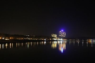 Illuminated city by river against sky at night