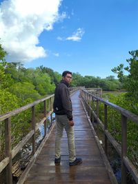 Man standing on footbridge against sky