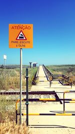 Road sign by railroad tracks against clear blue sky