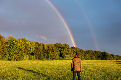 Rear view of man standing on field against rainbow in sky