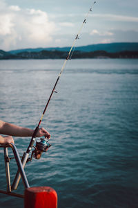 Man fishing in sea against sky during sunset