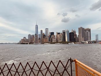 View of modern buildings by sea against cloudy sky