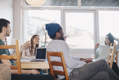 Young friends discussing while sitting against window in college dorm