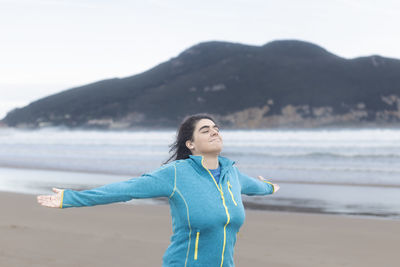 Happy mature woman opening her arms to the wind on the beach