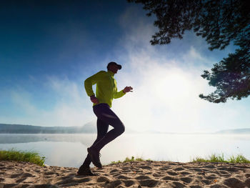 Slim man jogging on the beach early morning. runner in yellow black running suit run along lake.