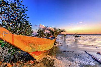 Boat moored in sea against sky during sunset