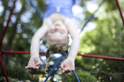 Cute girl hanging upside down on jungle gym against trees at playground