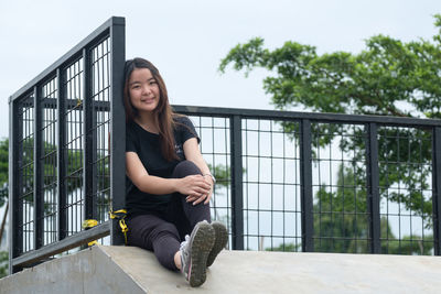 Portrait of smiling young woman sitting on steps against sky