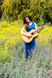 Beautiful woman playing guitar while standing amidst flowers