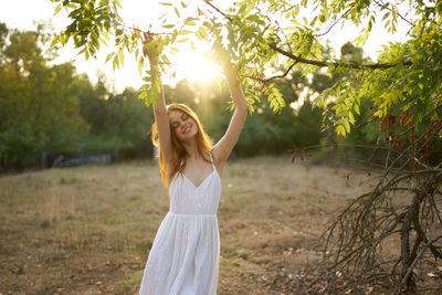 Woman standing by tree in sunlight
