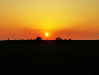 Scenic view of silhouette field against orange sky