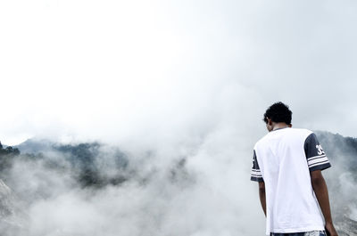 Rear view of man standing on mountain in foggy weather against sky