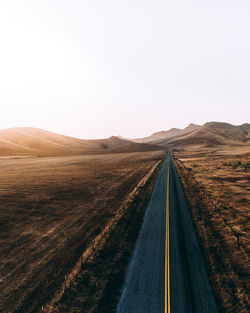 Road amidst land against clear sky