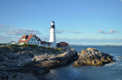 Lighthouse by sea and buildings against sky