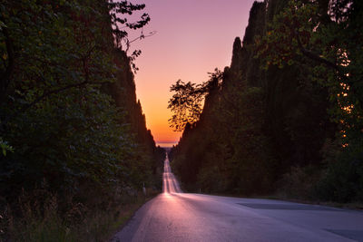 Empty road amidst trees against sky at sunset