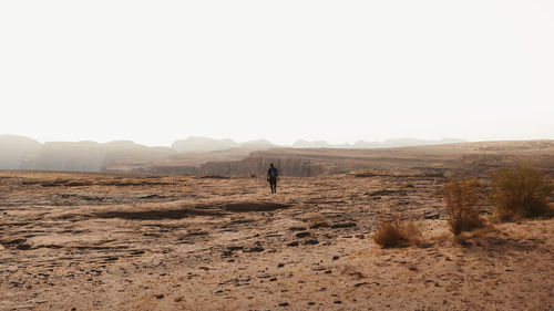 Rear view of woman walking at desert against clear sky