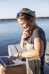Mid adult woman smiling while using laptop on pier