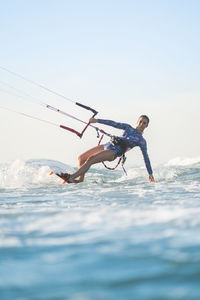 Side view of fit female kite surfer in swimsuit ridding waves in sea on sunny day in summer