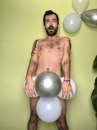 Portrait of shirtless man with balloons against wall