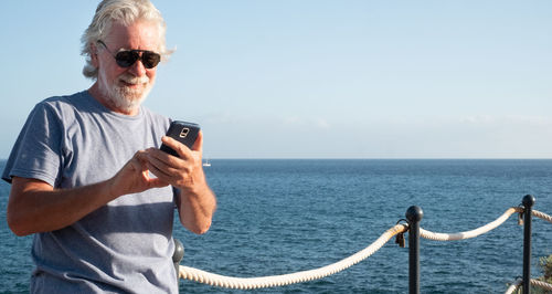 Smiling senior man using mobile phone while standing at sea 