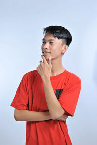 Handsome young asian boy wearing orange t-shirt with hand on chin thinking about question, pensive expression. smiling with thoughtful face. doubt concept