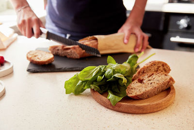 Woman hands is cutting a french baguette in the kitchen. basil and whole grain cutting bread. 