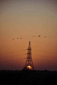 Low angle view of birds flying against orange sky