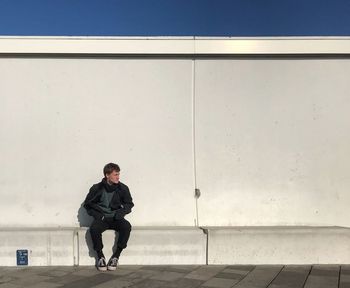 Full length of man sitting against wall