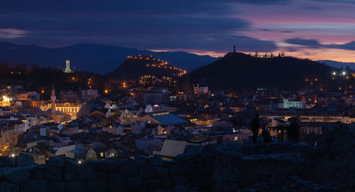 Illuminated buildings in town against sky at sunset