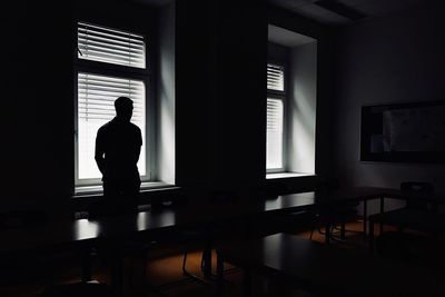 Rear view of silhouette man standing by window at home