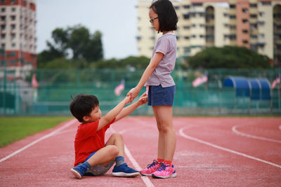 Girl giving helping hand to friend fallen on running track