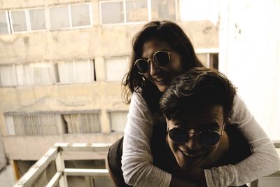 Portrait of happy man piggybacking girlfriend at balcony