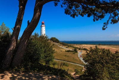 Lighthouse amidst trees and buildings against sky