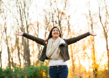 Portrait of young woman with arms raised standing in autumn