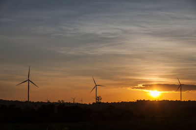 Silhouette wind turbines on field against sky during sunset