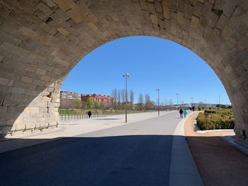 Road seen through arch against clear blue sky