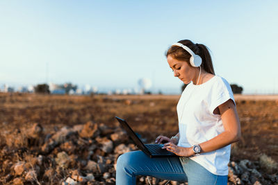 Young woman using laptop on land against sky