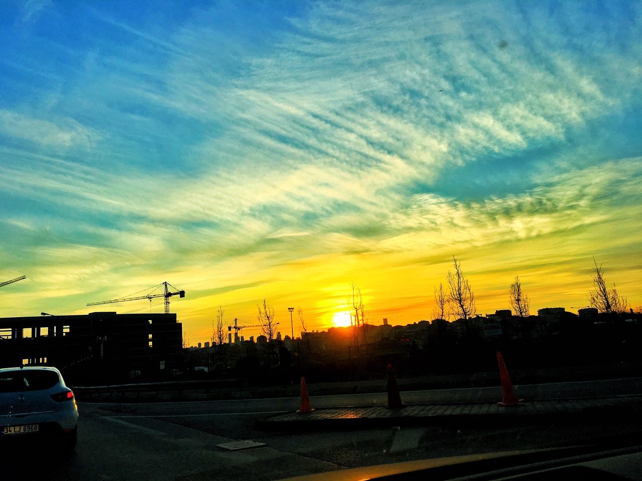 sunset, transportation, sky, car, orange color, land vehicle, road, mode of transport, silhouette, cloud - sky, electricity pylon, street, street light, power line, cloud, dramatic sky, nature, outdoors, no people, yellow