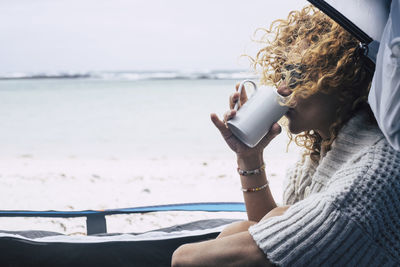 Woman drinking coffee while sitting at beach