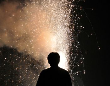 Rear view of silhouette man looking at firework against sky
