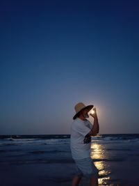 Optical illusion of man eating sun at beach against sky during sunset