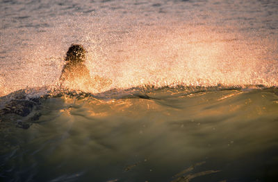 Water splashing on silhouette girl in sea during sunset