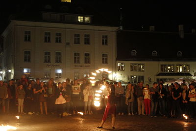 People standing on illuminated street against buildings at night