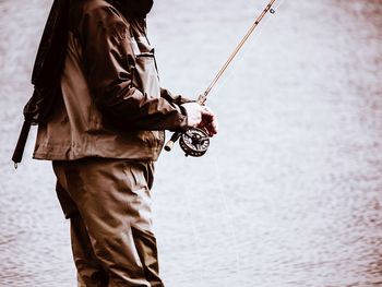 Midsection of man holding fishing rod by lake