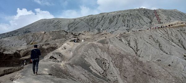 Rear view of man walking on mountain against sky