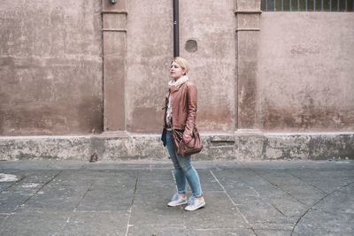 Full length portrait of smiling woman standing on footpath