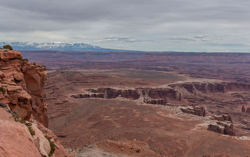 Panoramic high angle view of sandstone cliffs and formations in a canyon with snow capped mountains