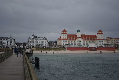 People on buildings by sea against sky in city