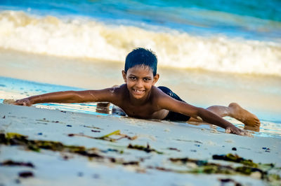 Portrait of shirtless boy smiling while lying at beach