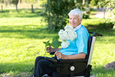 Portrait of young woman using mobile phone while sitting on field